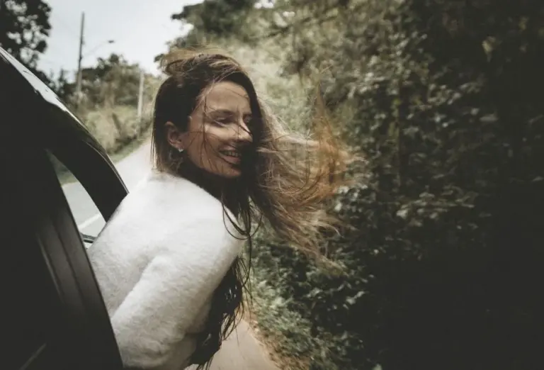 Mulher sorridente com o braço para fora da janela do carro