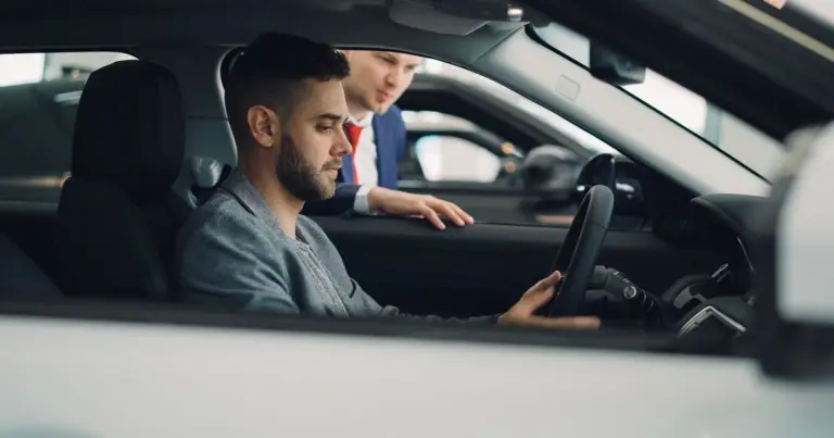 Vendedor em pé conversa com um comprador sentado dentro de um carro em uma loja