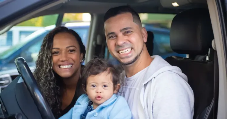 Família de três pessoas sorrindo dentro do carro