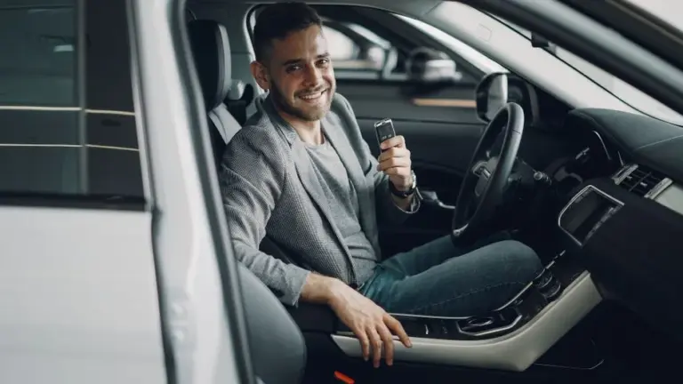 Homem sorridente segurando a chave dentro do carro novo