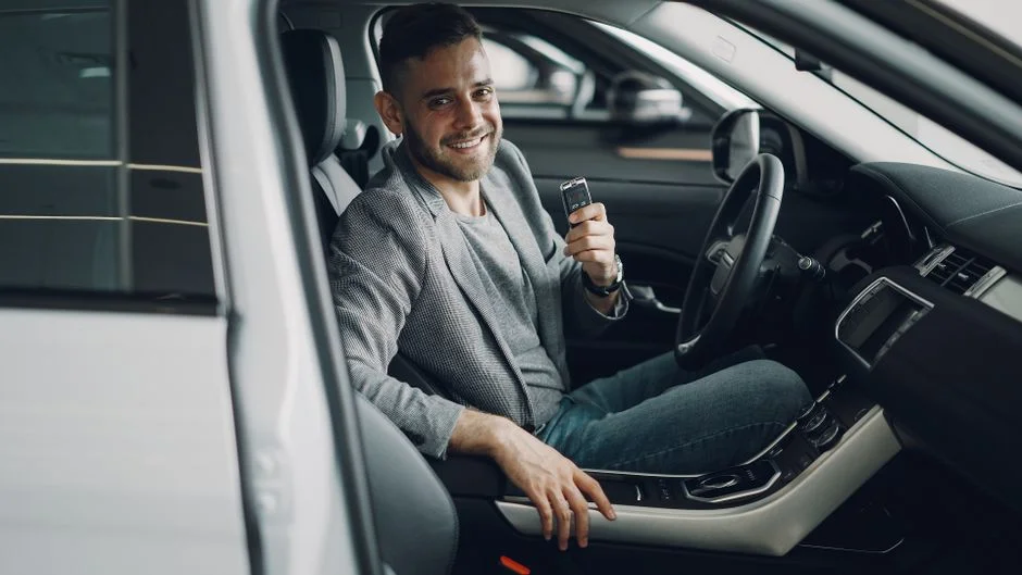 Homem sorridente segurando a chave dentro do carro novo