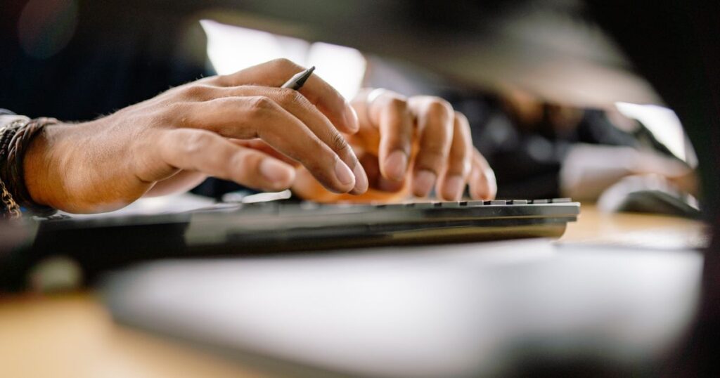 Mãos digitando em um teclado de computador.